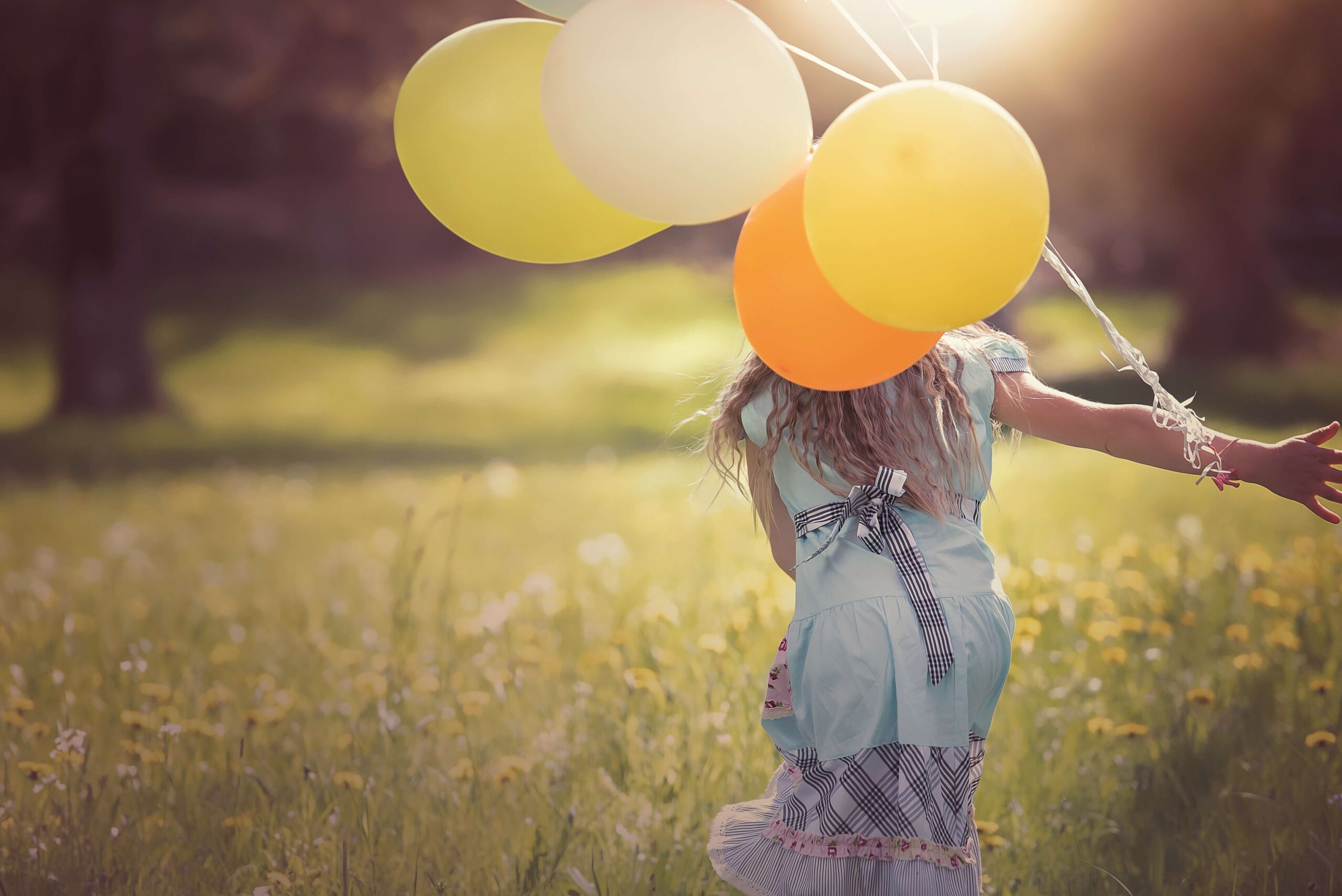 Eine junge Frau die ihre Emotionen erlaubt und voller Lebensfreude mit Luftballons über eine Wiese rennt.